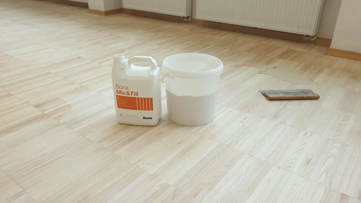 Posoda kita za fuge in vedro na zbrušenem svetlem parketu