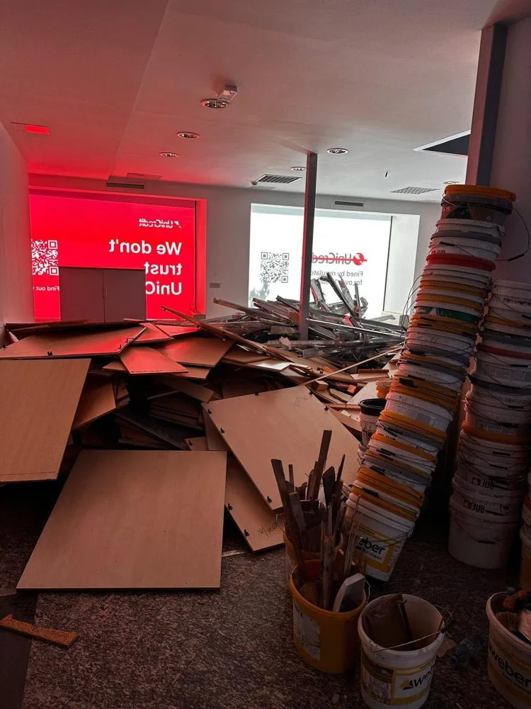 Notranjost poslovnih prostorov na Wolfovi 1 z osvetljeno rdečo opremo banke UniCredit in kupom demontiranih lesenih plošč.